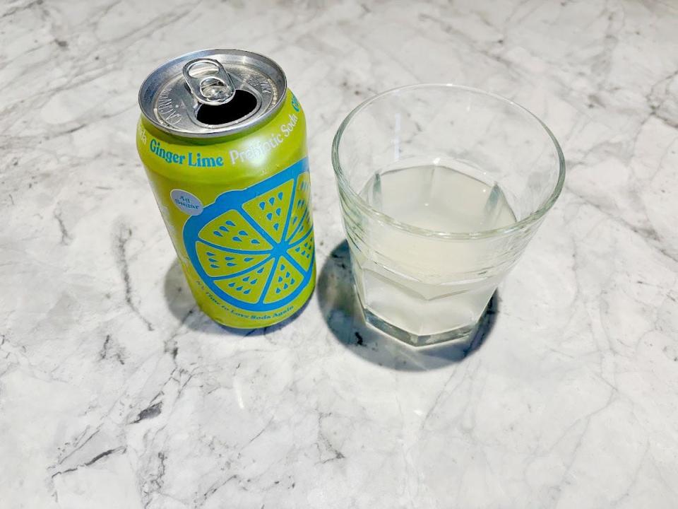 An open can of ginger-lime Poppi next to a small, clear glass with clear liquid inside. Both are sitting on a countertop.