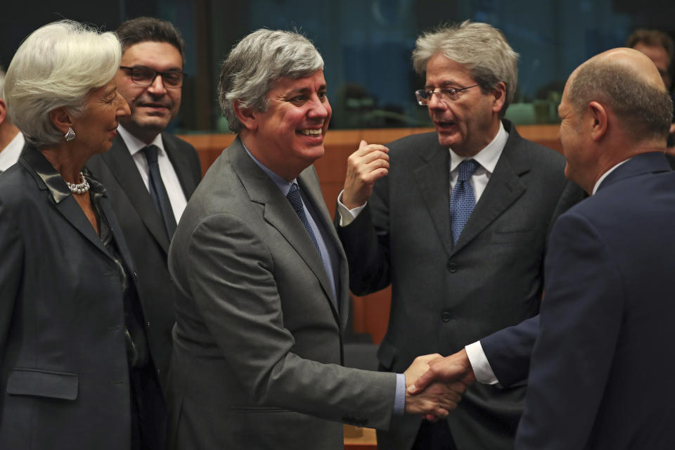 FILE - In this Monday, Jan. 20, 2020 file photo Eurogroup President Mario Centeno, center, shakes hands with German Finance Minister Olaf Scholz, right, next to European Central Bank President Christine Lagarde, left, Cyprus' Economy Minister Constantinos Petrides, second left, and European Commissioner for Economy Paolo Gentiloni, second right, during a meeting of European Union Finance Ministers in Eurogroup format at the Europa building in Brussels. Governments from the 19 countries that use the euro overcame sharp differences to agree Thursday on measures that could provide more than a half-trillion euros ($550 billion) for companies, workers and health systems to cushion the economic impact of the virus outbreak. Mario Centeno, who heads the finance ministers' group from euro countries, called the package of measures agreed upon "totally unprecedented... Tonight Europe has shown it can deliver when the will is there." (AP Photo/Francisco Seco, File)