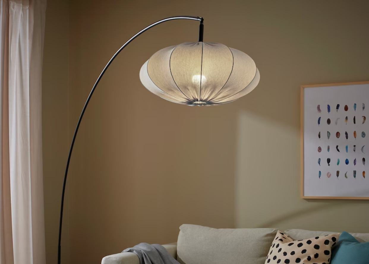  An arched floor lamp with a light blue textile shade overhanging a sofa. 