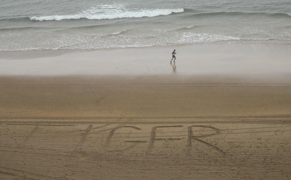 A runner jogs past 'Tiger' written in the sand on the beach below Portrush golf course as golfers compete in the first round of the British Open Golf Championships at Royal Portrush in Northern Ireland, Thursday, July 18, 2019.(AP Photo/Peter Morrison)