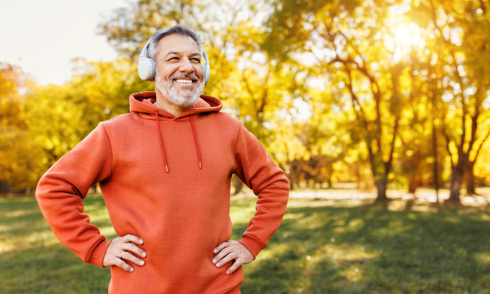 Portrait of happy positive mature man with broad smile  in headphones while doing sport in city park, active retired male sportsman jogging outside in early morning. Healthy lifestyle concept