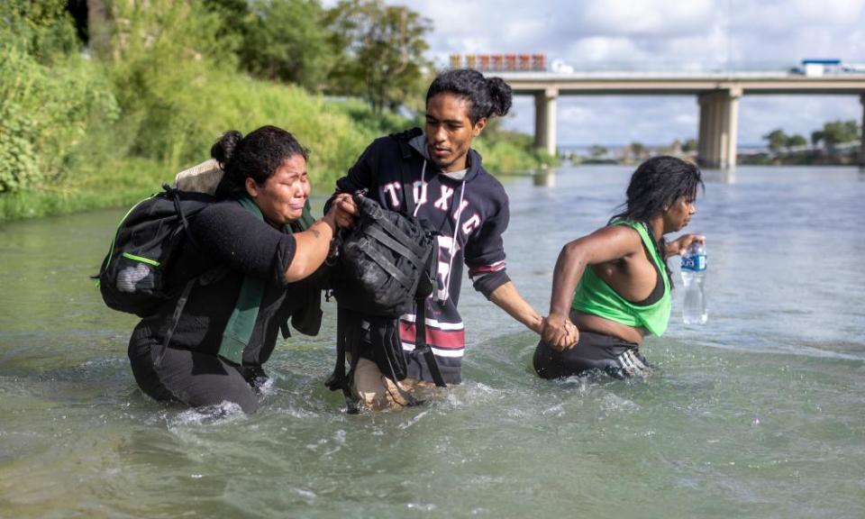 Three people, one crying, wade waist deep in a river, holding hands.