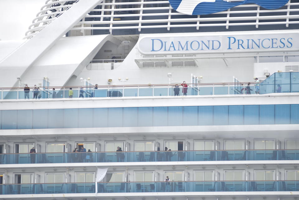 YOKOHAMA, JAPAN - FEBRUARY 15 : Passengers, wearing mask against the coronavirus, are seen on the deck and balconies of Diamond Princess cruise ship docked and in quarantine at the Daikoku Pier Cruise Terminal in Yokohma, Japan on February 15, 2020. Japan still continues to report several case of people infected by the coronavirus Covid-19 since the start of outbreak as well as on board the Diamond Princess cruise ship quarantined in Yokohama Bay for around 15 days. On February 15, during a press conference, Japan's Health Minister said that 67 more people on board of the cruise ship have been infected. (Photo by David Mareuil/Anadolu Agency via Getty Images)