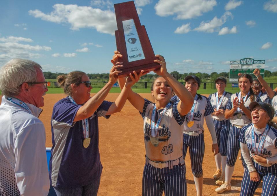 Spanish River High School Head Coach Head Coach Ashley Byrd, left center, and Isabella Santos, (42), hoist the State Championship trophy as they celebrate the team’s victory over Plant High School during their FHSAA State 7A Championship softball game at the Legends Way Ball Fields in Clermont Saturday. At left is retiring school Athletic Director Kevin McEnroe. May 27, 2023.