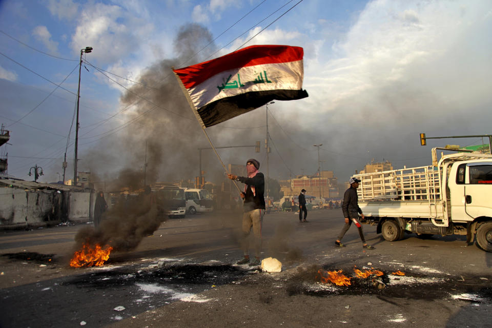 A protester waves the Iraq flag while demonstrators set fire to close streets near Tahrir Square during a demonstration to protest against the Iranian missile strike in Baghdad, Iraq.