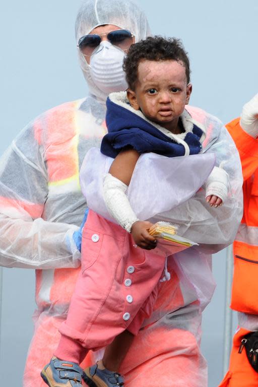 A rescuer carries an injured child as migrants disembark in the Italian port of Salerno, on May 5, 2015