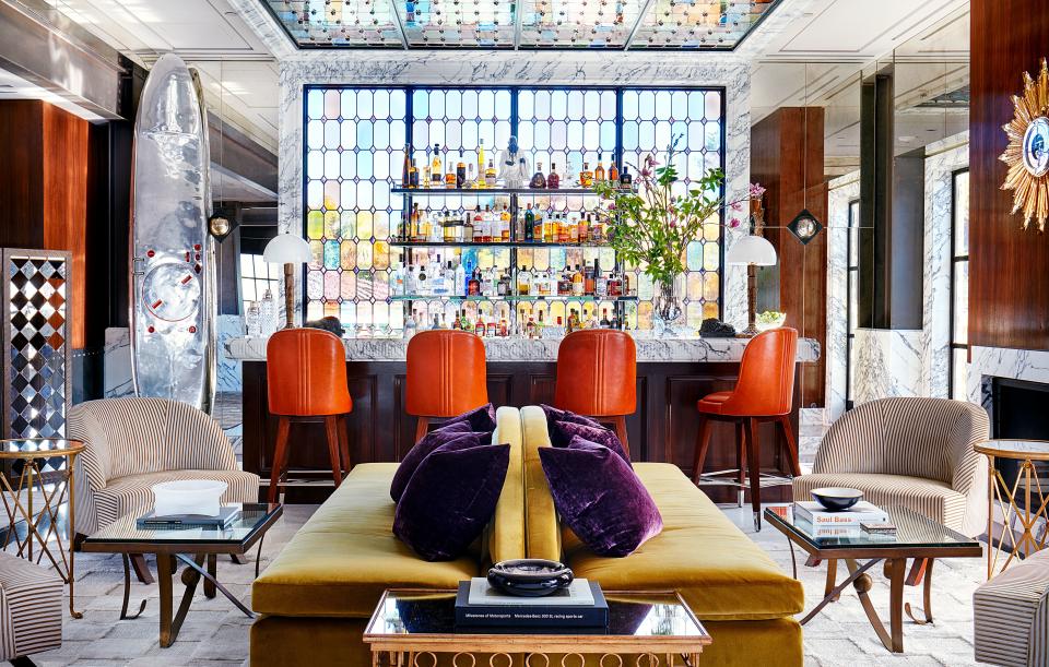 A bespoke stained-glass window by Judson Studios defines the bar. Custom stools in Ralph Lauren Home leather; custom sofas in a Schumacher velvet; custom barrel chairs in a striped noblis velvet. In back left corner, circa-1965 aluminum jetboard.