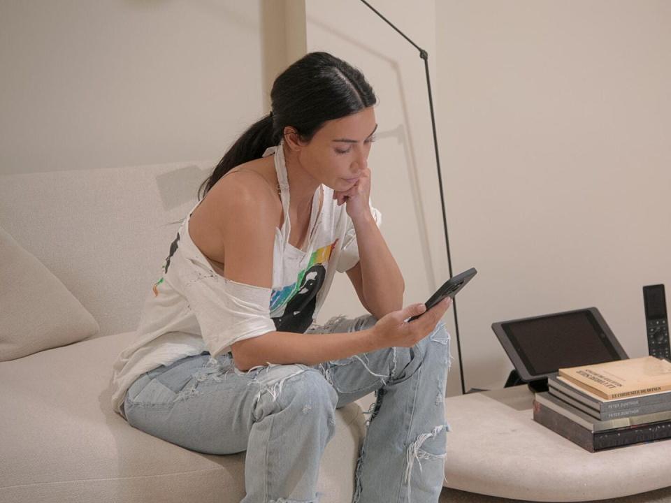 kim kardashian sitting on a couch, looking down at her phone with concern