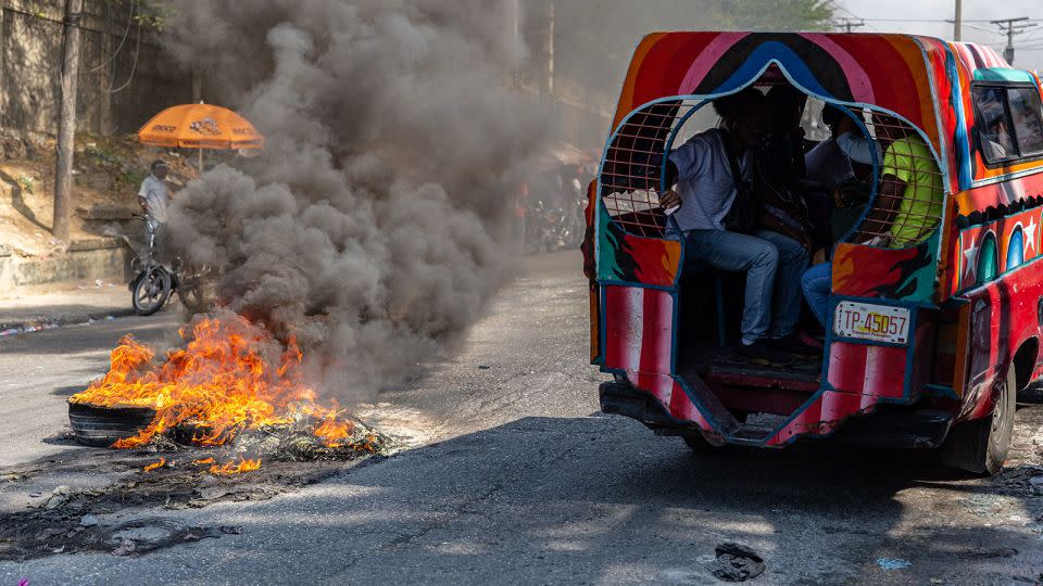 A public van passes burning tires left on a road Tuesday during a demonstration in the Haitian capital of Port-au-Prince. - Guerinault Louis/Anadolu/Getty Images