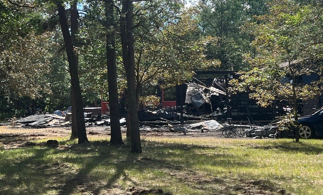 The blackened remains of a rented home in Necedah is seen from behind police tape Monday. Three adults and three children died early Sunday morning in a fire at the two-story home.