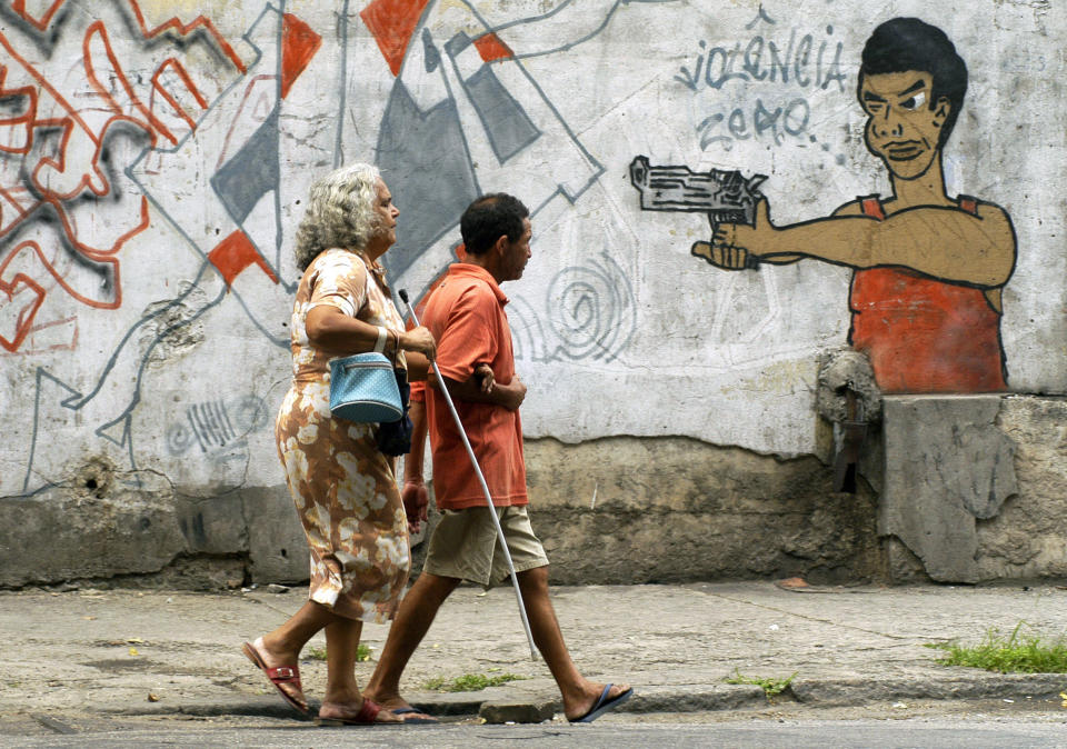 FILE - In this Oct. 22, 2005 file photo, people walk past graffiti in Rio de Janeiro, Brazil, a day before a vote to ban the sale of firearms and ammunition to civilians. Backed by the Roman Catholic church and other powerful forces in the country, one poll a month before the referendum put support at 73 percent. The U.S.-based National Rifle Association worked with activists in Brazil to help defeat it. (AP Photo/Renzo Gostoli, File)