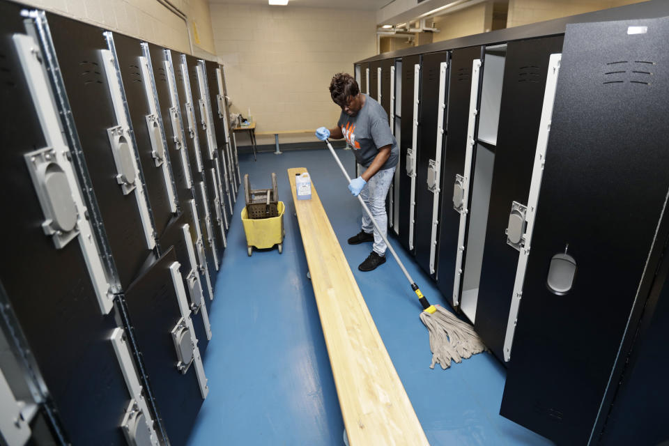 Custodian Joan Garner washes the floor in the pool locker room at Orange High School, Monday, March 16, 2020, in Pepper Pike, Ohio. Ohio Gov. Mike DeWine on Thursday ordered every school in Ohio to close for three weeks beginning at day's end Monday. DeWine says it's possible Ohio schools may be closed for the rest of the academic year. (AP Photo/Tony Dejak)
