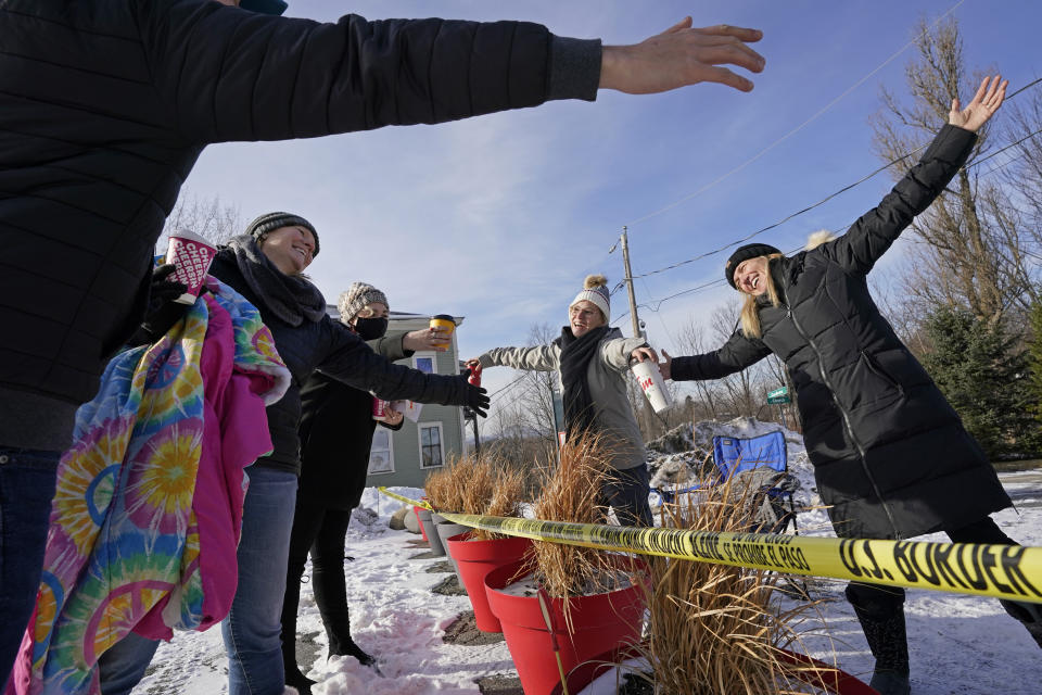 Las canadienses Stephanie Frizzell, a la derecha, y su hija, Shelby Dubois, segunda desde la derecha, se acercan para intercambiar un abrazo con sus parientes estadounidenses, Christian Gervais, a la izquierda, Sherie Frizzel, segunda desde la izquierda, y Caitlin Davis, tercera desde la izquierda, el sábado 19 de diciembre de 2020 en la frontera entre Estados Unidos y Canadá, marcada por una cinta amarilla en Stanstead, Quebec, y Derby Line, Vermont. (AP Foto/Elise Amendola)