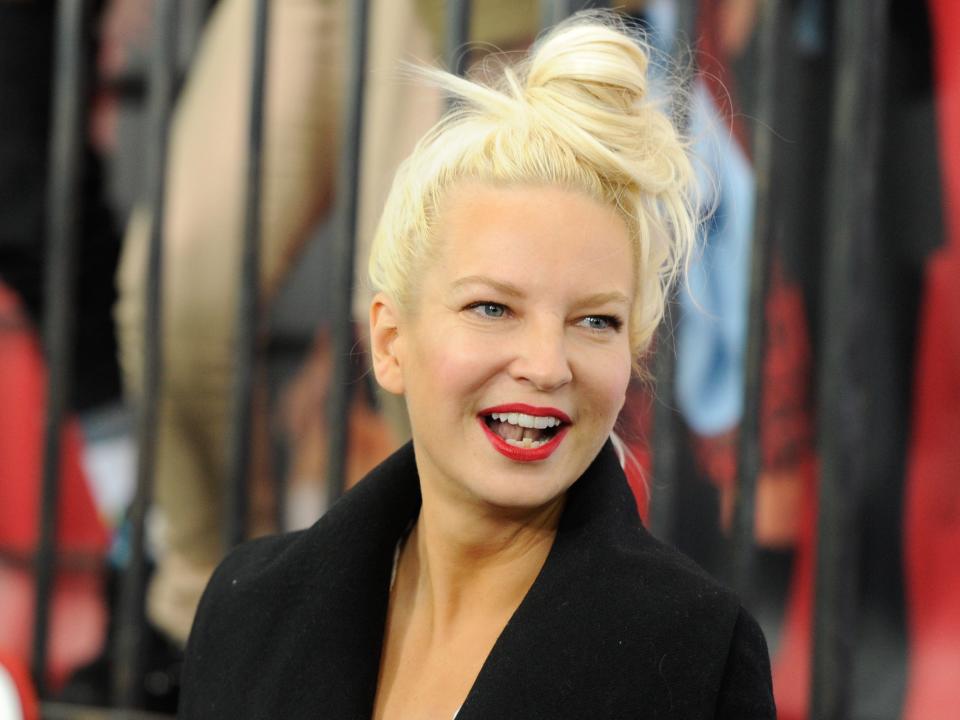 Sia smiling with her hair up in a bun and jacket on.