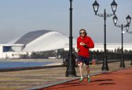 A man jogs along a coastline during a sunny day as the Olympic Park is seen on background during the 2014 Winter Olympic Games in Sochi February 12, 2014. REUTERS/Shamil Zhumatov