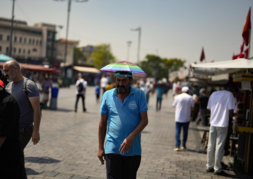 A man wears an umbrella hat to shelter from the sun as he walks in in Eminonu district in Istanbul, Turkey, Thursday, July 20, 2023. (AP Photo/Khalil Hamra)