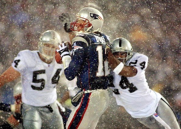 FOXBORO, UNITED STATES:  New England Patriots  quarterback Tom Brady (C) takes a hit from Charles Woodson (R) of the Oakland Raiders on a pass attempt in the last two minutes of the game in their AFC playoff 19 January 2002 in Foxboro, Massachusetts.  The Patriots won 16-13 in overtime. AFP PHOTO/Matt CAMPBELL (Photo credit should read MATT CAMPBELL/AFP via Getty Images)