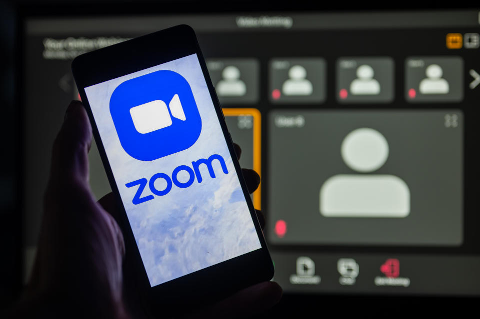 O logotipo do Zoom é exibido no smartphone com a tela do Zoom em segundo plano. 