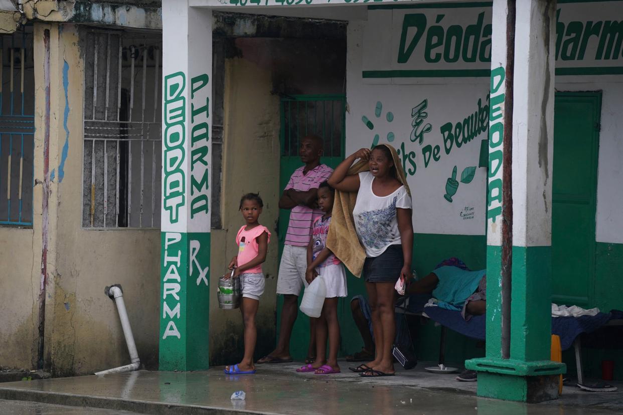 Earthquake-displaced people stand under a pharmacy's overhang the morning after Tropical Storm Grace swept over Les Cayes, Haiti, Tuesday, Aug. 17, 2021, three days after a 7.2-magnitude earthquake.