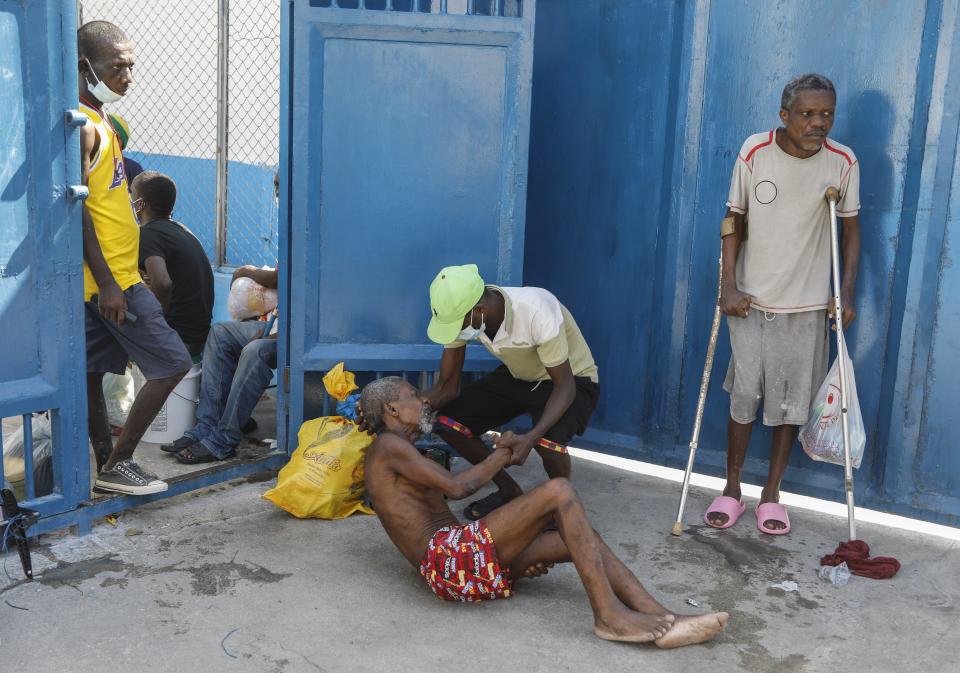 An inmate comes to the aide of a prisoner after armed gangs freed thousands from the National Penitentiary, in Port-au-Prince, Haiti, Saturday, March 3, 2024. (AP Photo/Odelyn Joseph)