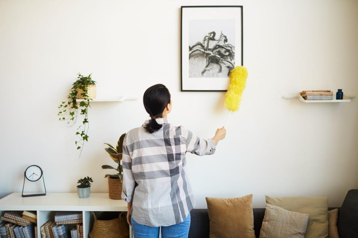 Woman dusting walls before cleaning