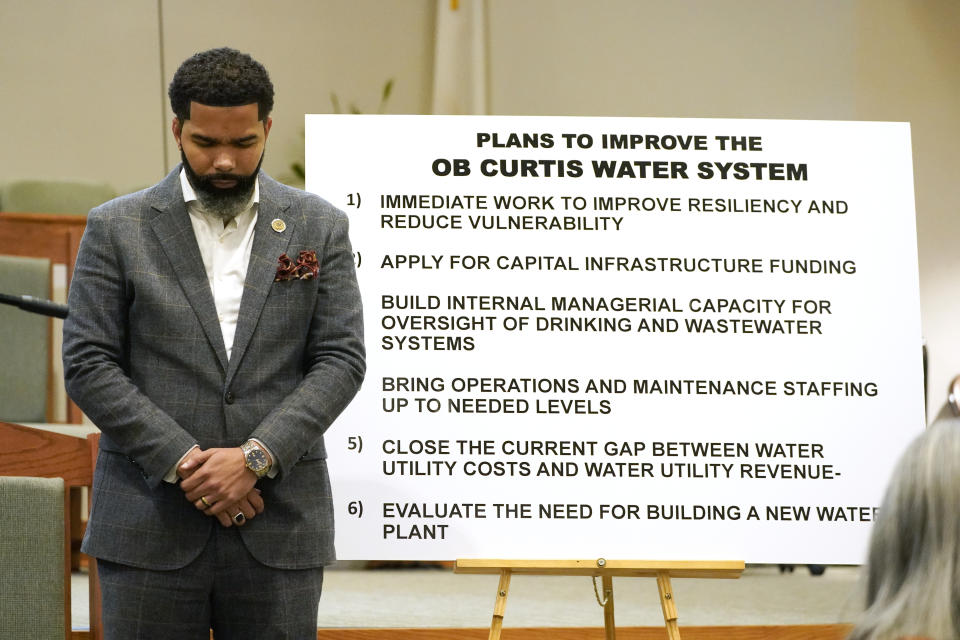 Mayor Chokwe Antar Lumumba stands in prayer near a poster outlined with plans for improving the primary water system plant, on Tuesday, Sept. 13, 2022, at the start of a community meeting at College Hill Missionary Baptist Church, Jackson, Miss. It was held to update the public on the current water system situation. (AP Photo/Rogelio V. Solis)