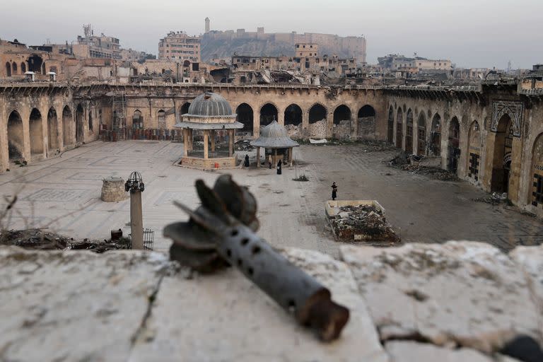 Archivo - Un mortero en primer plano mientras abajo la gente visita la mezquita de Gran Omeya, dañada gravemente, con la ciudadela de la ciudad siria de Alepo al fondo