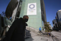 A man walks by the logo of Tokyo Olympic Games planned to start in the summer of 2021, in Tokyo, Tuesday, Jan. 19, 2021. Tokyo organizers have no public program planned to mark the milestone. There is too much uncertainty for that right now. Tokyo and other parts of Japan are under an emergency order because of surging coronavirus cases. (AP Photo/Koji Sasahara)