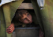 <p>An Afghan refugee boy Gul Zaman who fled from Afghanistan with his family, peeps from his make-shift tent in the outskirts of Karachi, Pakistan on March 13, 2012. (AP Photo/Shakil Adil) </p>