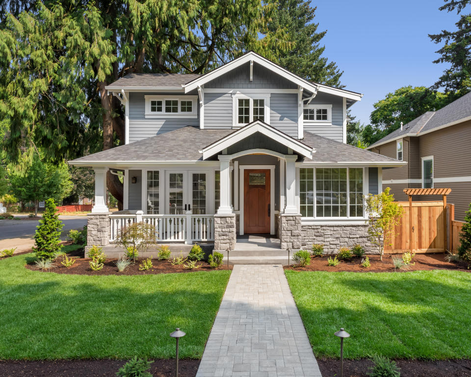 facade of home with manicured lawn, and backdrop of trees and blue sky