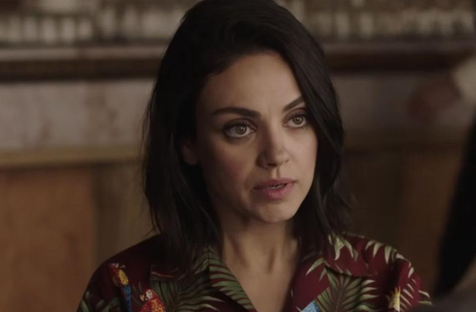 Mila Kunis in a hawaiian shirt talks to someone off-camera.