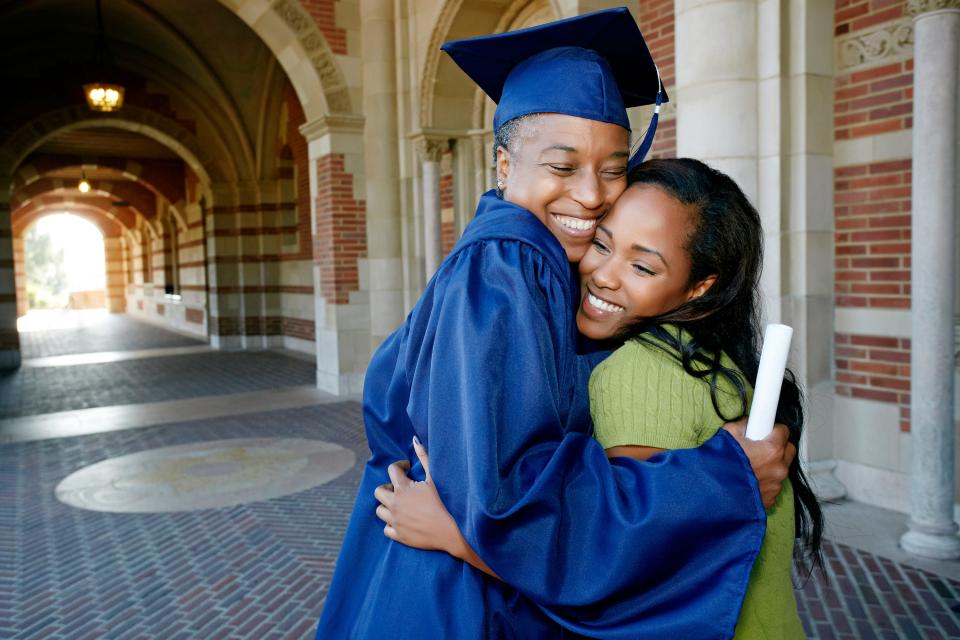 College graduate in blue cap and gown hugging their relative wearing a green shirt.
