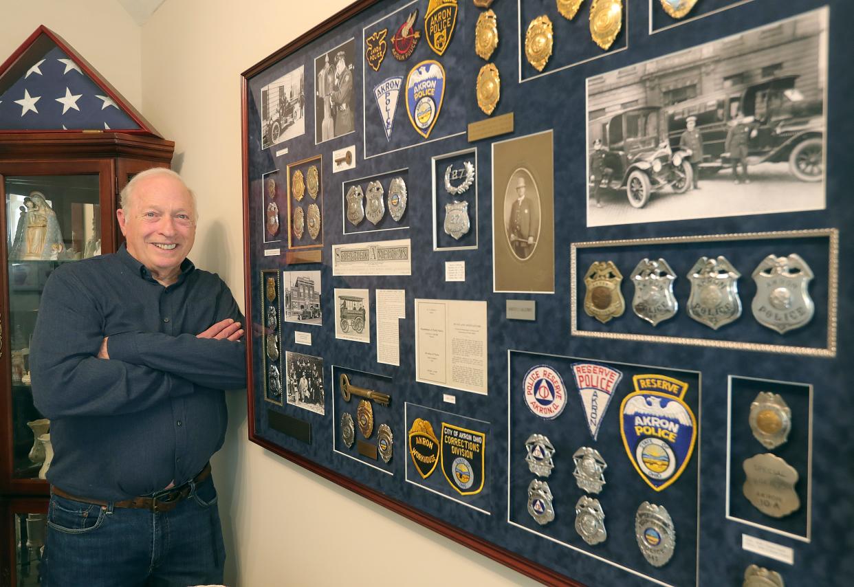 Tom Dye, a retired Akron police sergeant, stands next to some of the badges, patches and memorabilia he has collected.