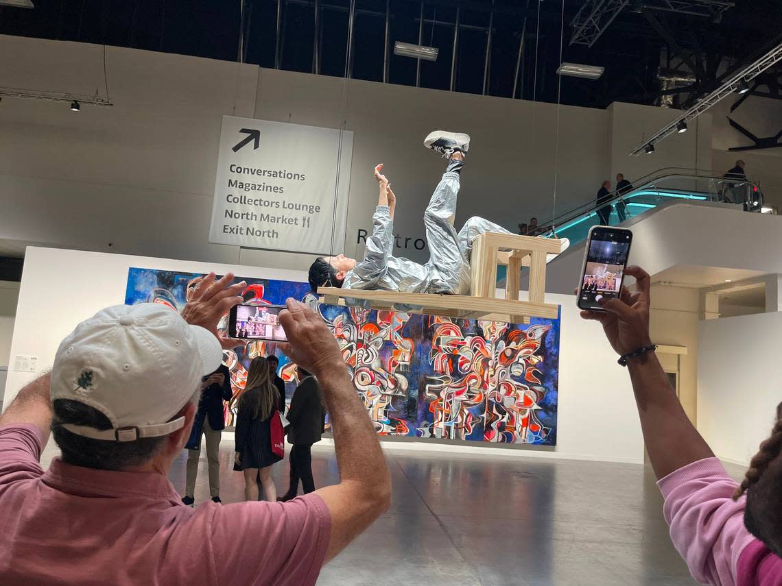 Visitors take video and photos of Colombian artist María José Arjona performing her piece “Chair” at Art Basel Miami Beach. During the hourslong performance, Arjona slowly moves her arms and legs as she reclines in a horizontal chair that is suspended several feet in the air.