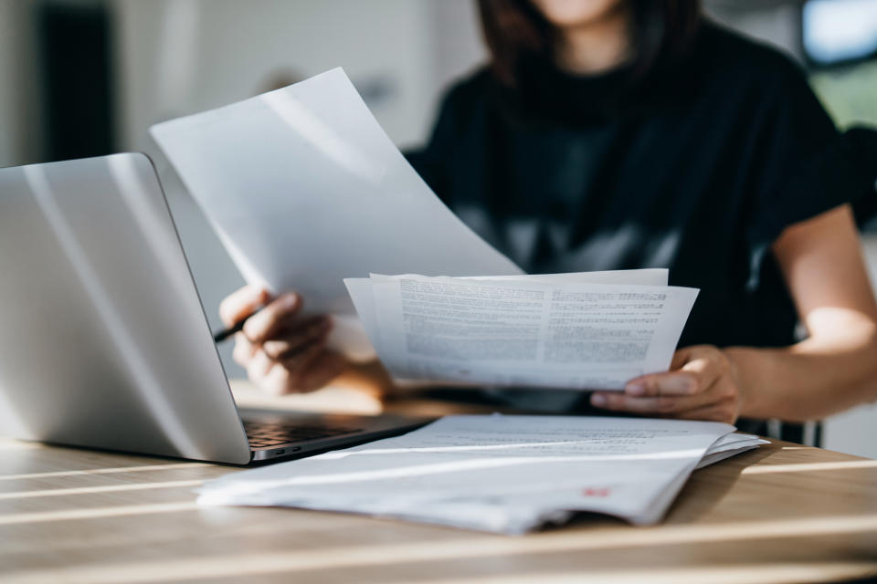 Person at a desk reviewing documents with an open laptop