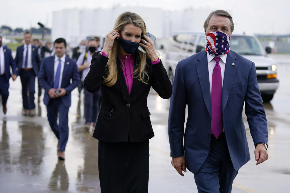 FILE- In this July 15, 2020, file photo Sen. Kelly Loeffler, R-Ga., puts on a face mask as she walks with Sen. David Perdue, R-Ga., right, at UPS Hapeville Airport Hub in Atlanta. (AP Photo/Evan Vucci, File)