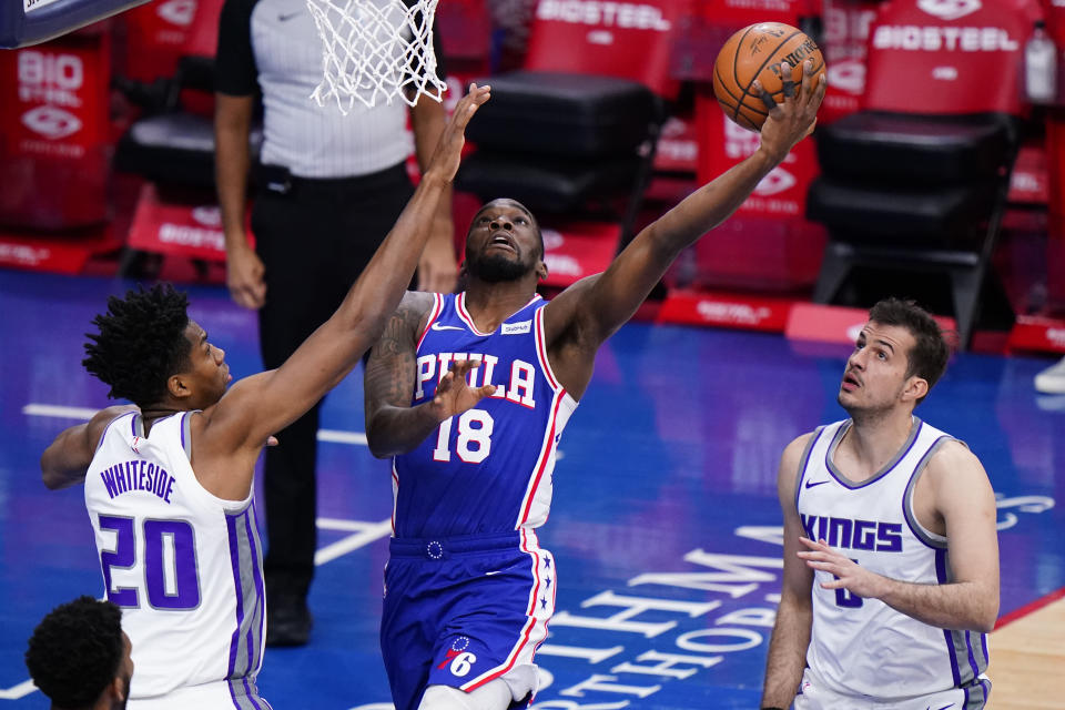 Philadelphia 76ers' Shake Milton, center, goes up for a shot between Sacramento Kings' Hassan Whiteside, left, and Nemanja Bjelica during the first half of an NBA basketball game, Saturday, March 20, 2021, in Philadelphia. (AP Photo/Matt Slocum)