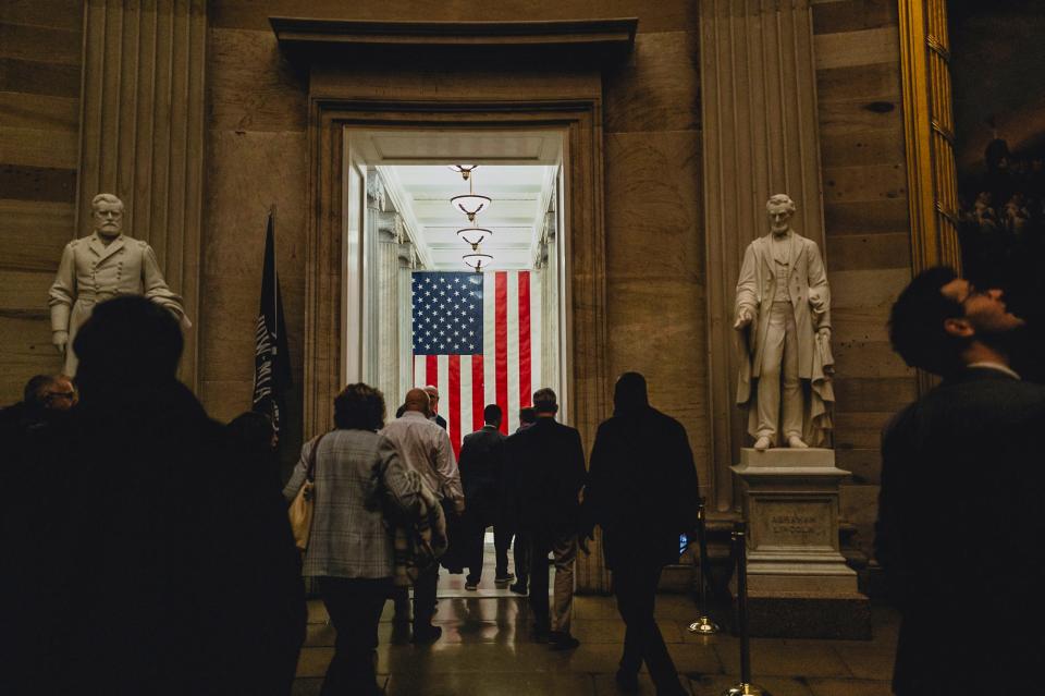 People walking through the Capitol interior with statues and paintings on the wall.