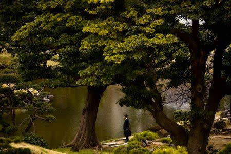 A businessman stands at a pond in the Kyu-Shiba-rikyu Garden on a warm and sunny day in Tokyo, Japan, March 18, 2016. REUTERS/Thomas Peter/File Photo