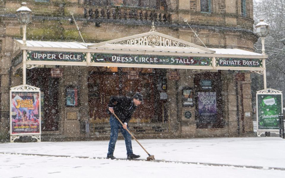 The owner of the Opera House in Buxton, Derbyshire is pictured clearing the snow from the entrance