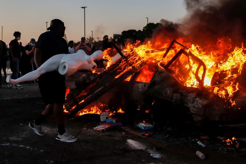 A man prepares to throw a mannequin onto a burning car at the parking lot of a Target store during protests in Minneapolis