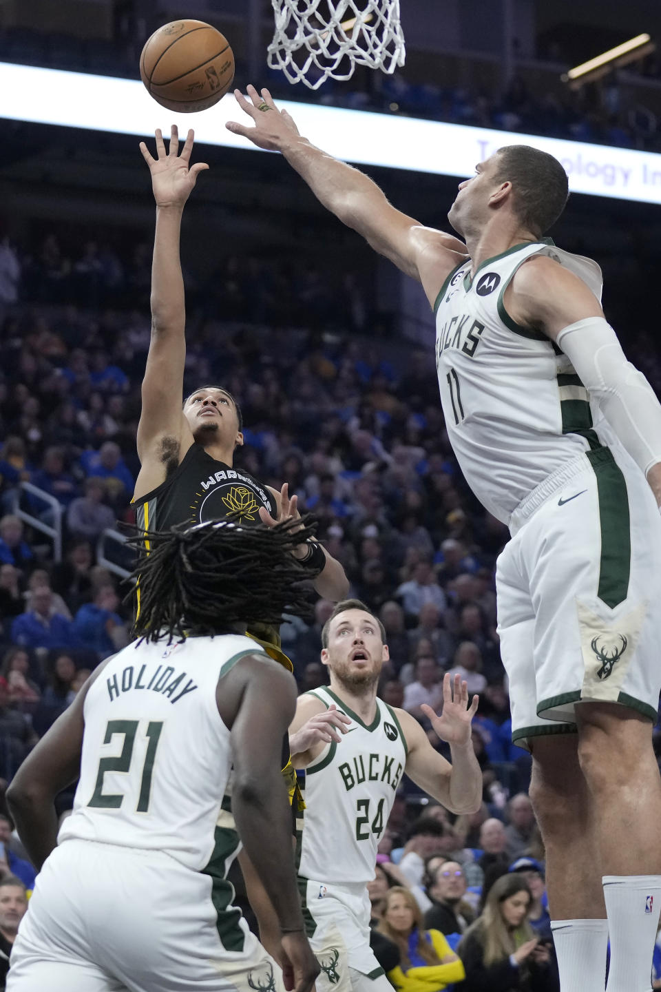 Golden State Warriors guard Jordan Poole, top left, shoots against Milwaukee Bucks guard Jrue Holiday (21), guard Pat Connaughton (24) and center Brook Lopez (11) during the first half of an NBA basketball game in San Francisco, Saturday, March 11, 2023. (AP Photo/Jeff Chiu)