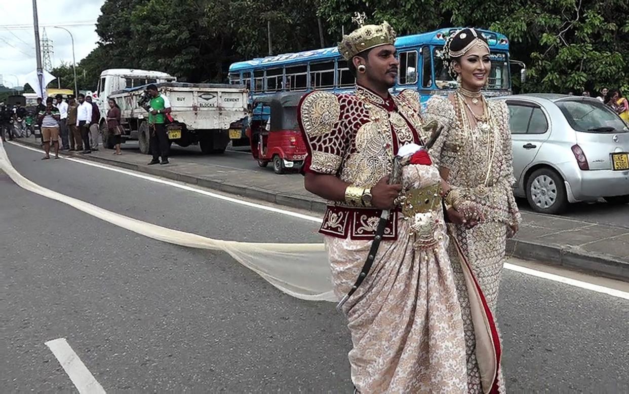 The Sri Lankan wedding couple walk along a road as as a bride attempts to set a record for the longest wedding saree - AFP