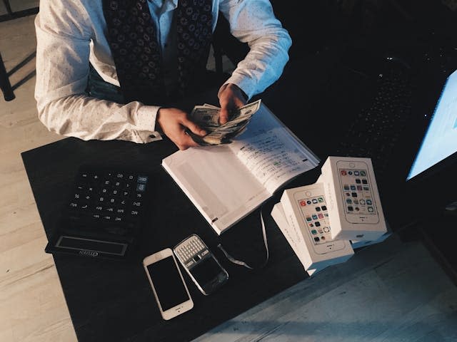 Man counts money at desk with a calculator and notebook nearby