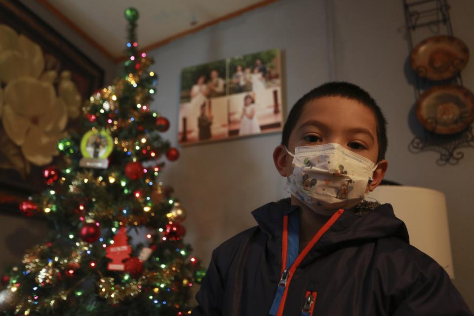 Angel, 6, poses in front of a Christmas tree at his home on Wednesday, Dec. 23, 2020, in Santa Fe, N.M. Angel's parents, both cooks, struggled to pay rent this year as their hours were cut in half. As immigrants in the country without work permission, they're ineligible for state unemployment or federal stimulus money. (AP Photo/Cedar Attanasio)