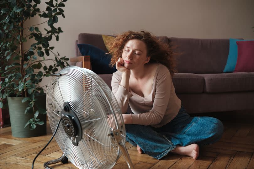 Overheated woman suffering from summer heat at home, using electric fan