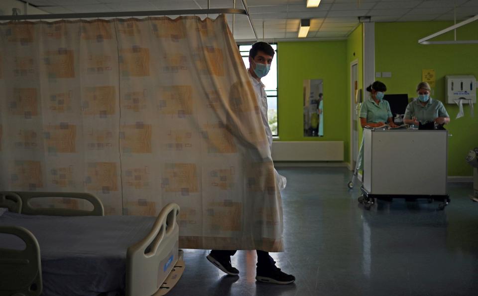 Stroke therapy worker Cavan Smith pulls the curtains around a patient's bed on the Acute Stroke Unit at the Royal Blackburn Teaching Hospital in Blackburn, north-west England on May 14, 2020, as national health service staff in Britain fight the novel coronavirus COVID-19 pandemic.