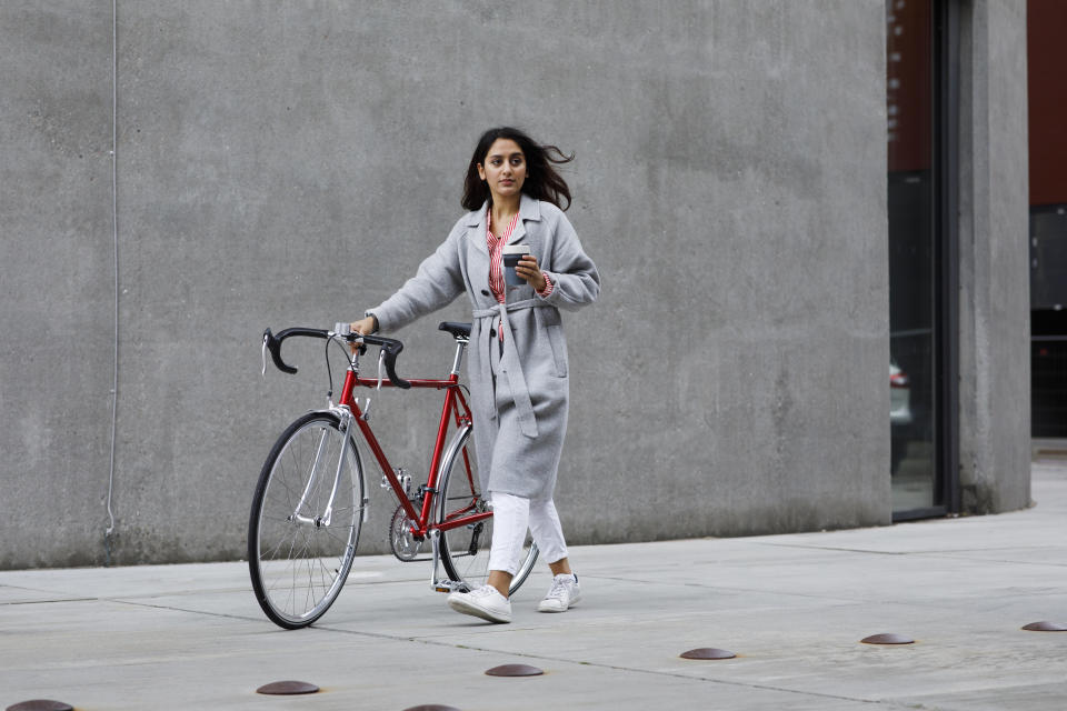 Woman walking to the office with a bike and coffee