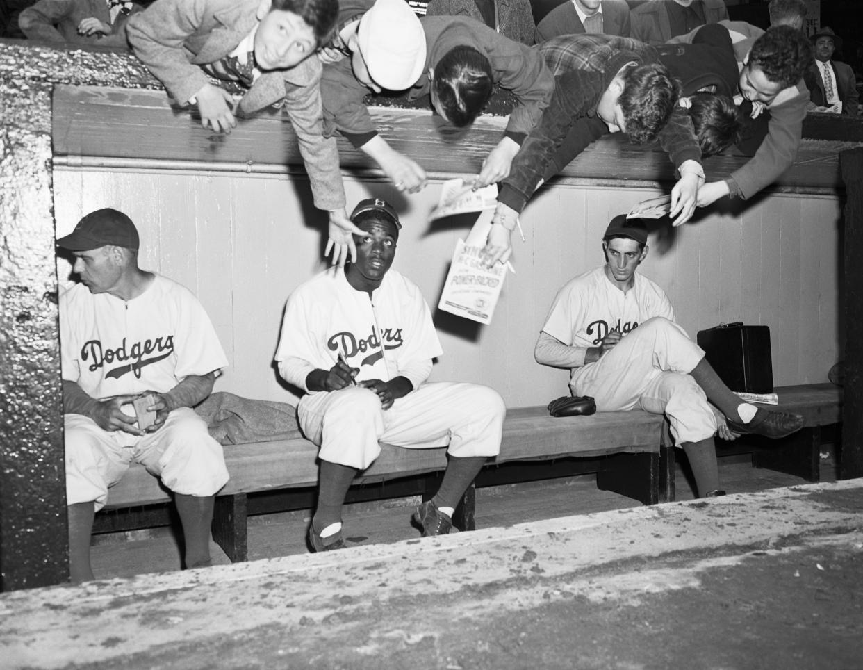 (Original Caption) 4/11/1947-New York, NY: Youthful Brooklyn Dodger's rooters and fans, reach over from behind the dugout at Ebbets field today, trying to get an autograph from Jackie Robinson, the first Negro ever to reach the Major League, joined the Brooklyn team, yesterday. He came from the Montreal team, The Dodgers played an exhibition game against the New York Yankees today.