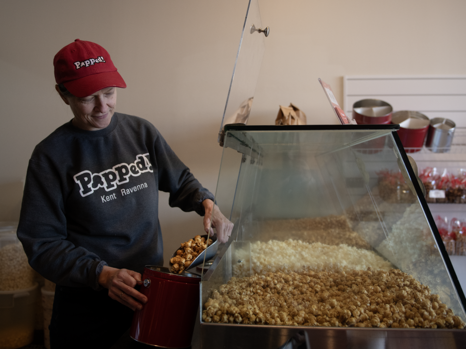 Gwen Rosenberg, founder and co-owner of Popped!, fills a holiday gift tin of caramel popcorn available at the Kent and Ravenna shops.